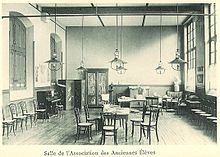 Photographie de la salle de l'AAE à la fin du XIXe siècle : il y a des meubles, un piano et un buste de Molière.