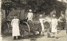 Des soldats allemands, en tabliers blancs et toques, posent pour le photographe autour de charrettes munies d’énormes roues ; de la vapeur s’élève de la seconde charrette.