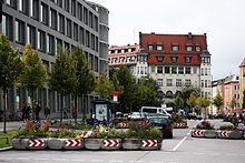 Large rue au milieu de laquelle ont été installés trois rangées de bacs amovibles en béton d'environ deux mètres garnis de plantes et de fleurs, afin de former une chicane pour canaliser la circulation automobile.