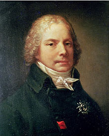 Portrait d'un homme, montrant sa tête et ses épaules. Il porte une veste noire avec un col montant très haut et une chemise blanche fermée par un nœud. Sa tête s'orne d'une perruque blonde et bouclée.