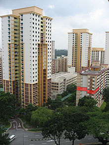 La photographie montre des immeubles d'habitation. Deux d'entre eux, au centre et à gauche, font 26 étages ; les autres sont plus petits. Un des appartements d'un immeuble sur la droite est coloré en rouge sur l'image pour être mis en avant.
