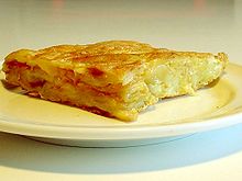 Gros plan sur un quart d’omelette dorée dont la coupe permet de voir les morceaux de pomme de terre enfouis dans la masse du mets.