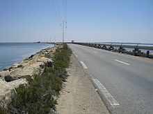 Perspective sur une route aménagée sur une digue entourée de part et d’autre par la mer ; un pipeline a été aménagé du côté droit.