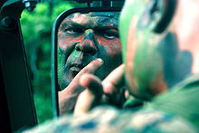 un homme se bariolant le visage de vert et brun