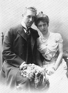 Photo du prince et de la princesse, assis côte à côte et penchés l’un vers l’autre, un bouquet de fleurs sur les genoux.