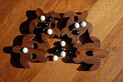Quatre formes de tortues sont découpées dans une planche de bois exotique. Chaque face de ces formes est percée de trous dans lesquels sont posées des billes en verre blanches ou noires