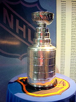 Photo de la coupe Stanley posée sur une table dont la nappe porte le logo de la LNH.