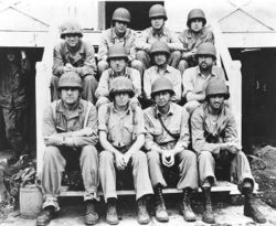 Black and white photo of eleven Marines in their combat uniforms sitting on some stairs