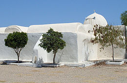 Façade de la mosquée Essatouri vue de l’extérieur et coiffée d’une coupole ; trois arbustes sont plantés au premier plan.