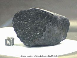 Un fragment de la météorite du lac Tagish aux côtés d'un cube d'un centimètre de côté.