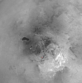 Ontario Lacus (en noir) et le pôle sud (croix rouge) de Titan vus par Cassini ; les nuages (taches claires) circulentdans le sens des aiguilles d'une montre.