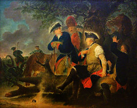 Four men are gathered under a tree. One, Frederick the Great, has his shirt sleeve rolled up and a second man is wrapping a bandage around his arm. A grenadier watches what he does. Another man in a tri-cornered hat stands at Fredrick's side. In the background, soldiers load and fire cannons.