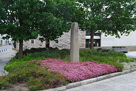 Le menhir de Plourin : Autrefois borne miliaire de la voie romaine. La mairie en arrière plan.