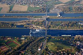 Le Rhin (au 1e plan), puis le canal séparé en 2 avec une écluse et, au fond, une centrale hydroélectrique.