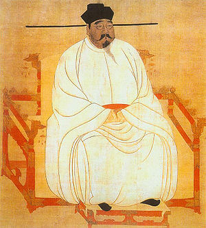 Peinture d'un homme corpulant assis sur un trône rouge décoré de têtes de dragons, vêtu d'une robe de soie blanche, de chaussures noires et d'un chapeau noir. Il porte une moustache et une barbiche