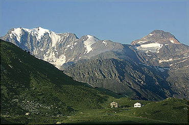 Photographie en couleur de montagnes aux sommets enneigés en arrière-plan, avec au premier plan de vertes collines.