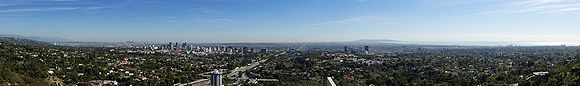 Photo en couleur, prise d'un point élévé, de Los Angeles ; on voit la ville au loin, au premier plan il y a de nombreux espaces verts arborés.