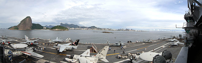 Vue panoramique des avions présents sur le pont d'envol du navire, et de la côte en arrière-plan.